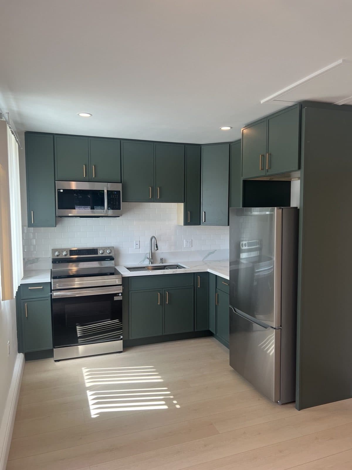 Finished ADU kitchen with deep green cabinets, stainless appliances, and quartz counters